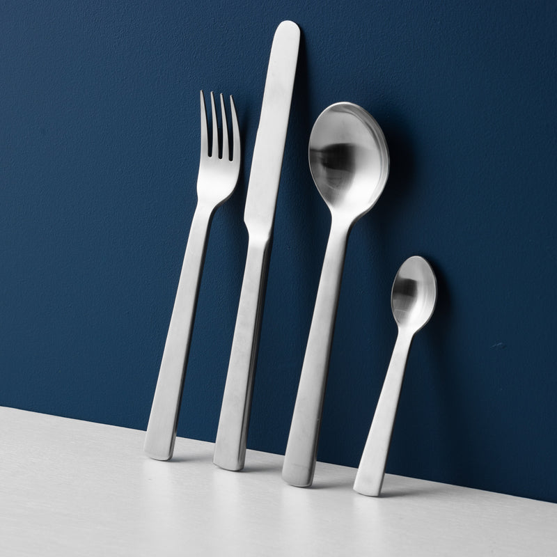 This image depicts Acme's brushed fork, knife, spoon and teaspoon against a navy blue background.